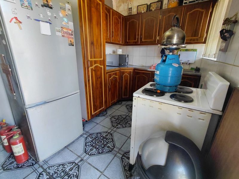 A compact kitchen featuring traditional wooden cabinetry, tiled flooring, and a tiled backsplash, offering a functional layout with potential for modern updates.