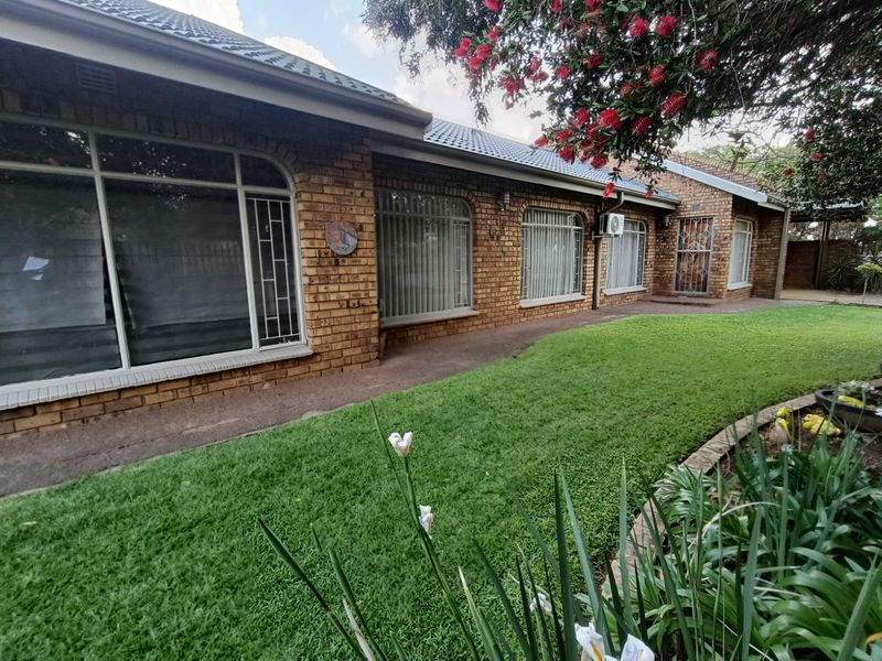 Rear view of a face brick house featuring a tiled roof, large arched windows with security bars, and a well-maintained lawn.
