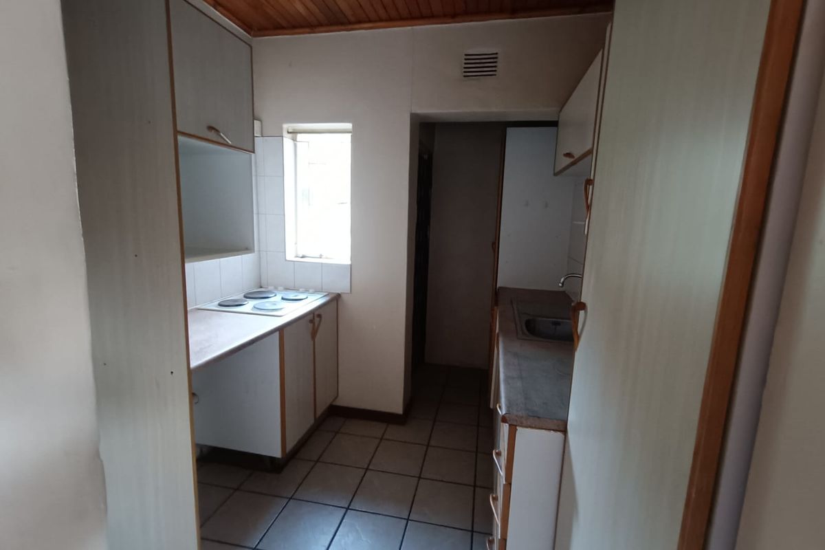 A compact, dated kitchen featuring built-in cabinetry, an electric hob, a stainless steel sink, and tiled flooring with a timber ceiling.
