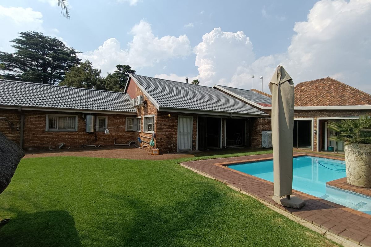 Rear view of the property featuring a facebrick facade, tiled roof, well-maintained lawn, and a swimming pool with brick paved surround.