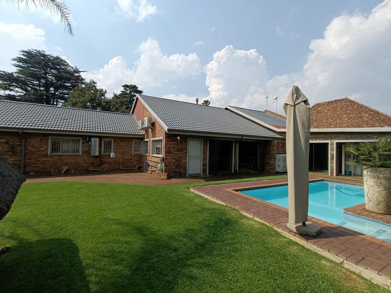 Rear view of the property featuring a facebrick facade, tiled roof, well-maintained lawn, and a swimming pool with brick paved surround.