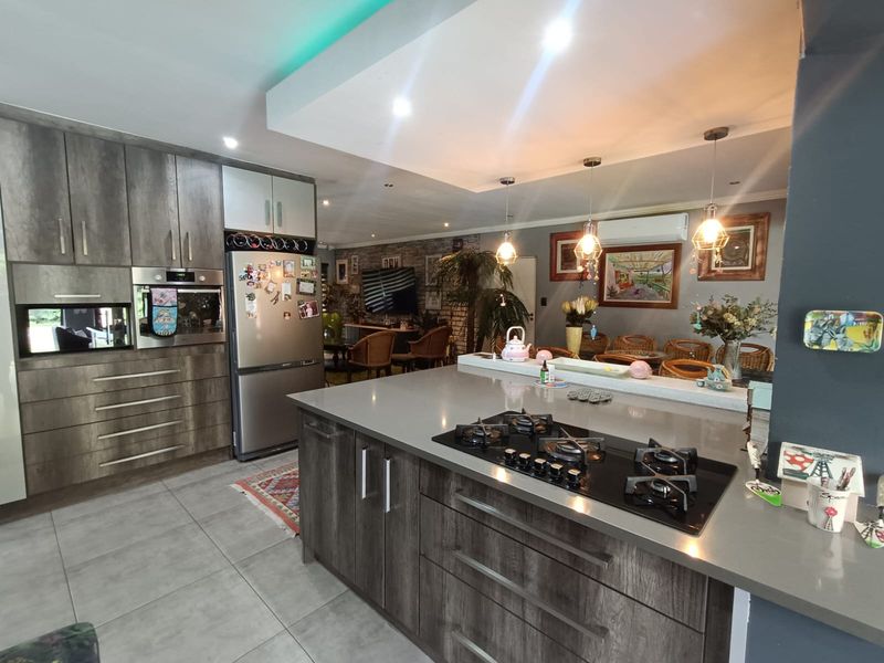 Modern open-plan kitchen featuring a central island with gas cooktop, stone countertops, built-in oven, and sleek cabinetry, flowing into the living and dining area.