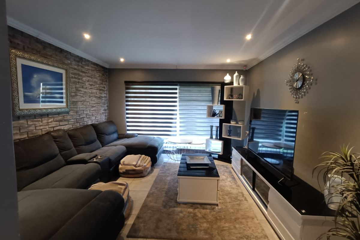 A well-maintained living room featuring an exposed brick accent wall, tiled flooring, and modern recessed downlighting.