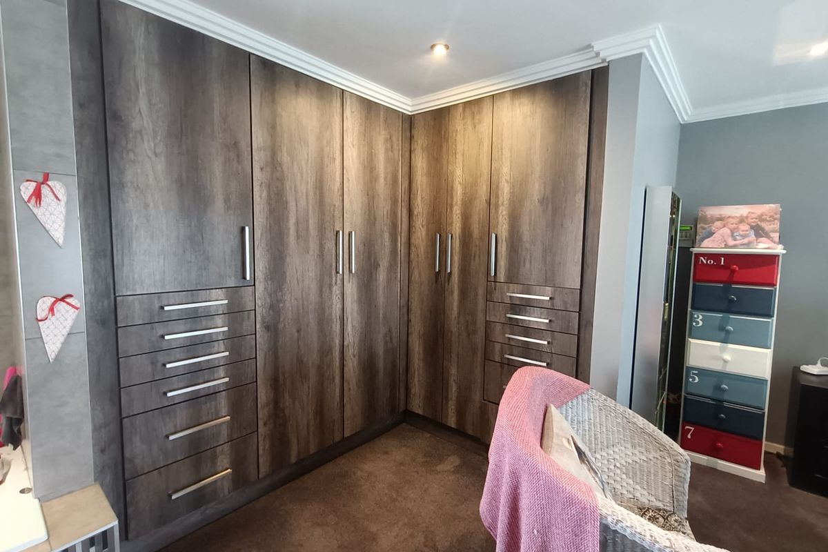 A bedroom featuring extensive dark wood-grain built-in cupboards with integrated drawers, recessed ceiling lighting, and crown molding detail.