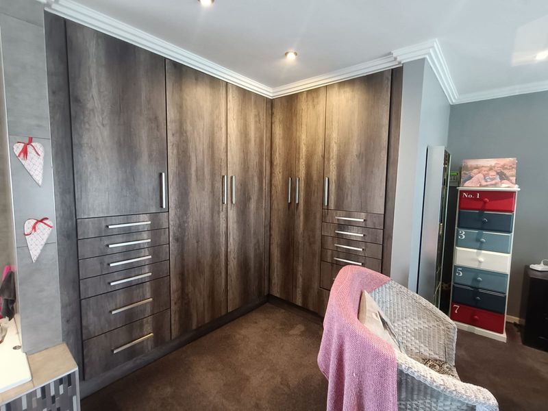A bedroom featuring extensive dark wood-grain built-in cupboards with integrated drawers, recessed ceiling lighting, and crown molding detail.