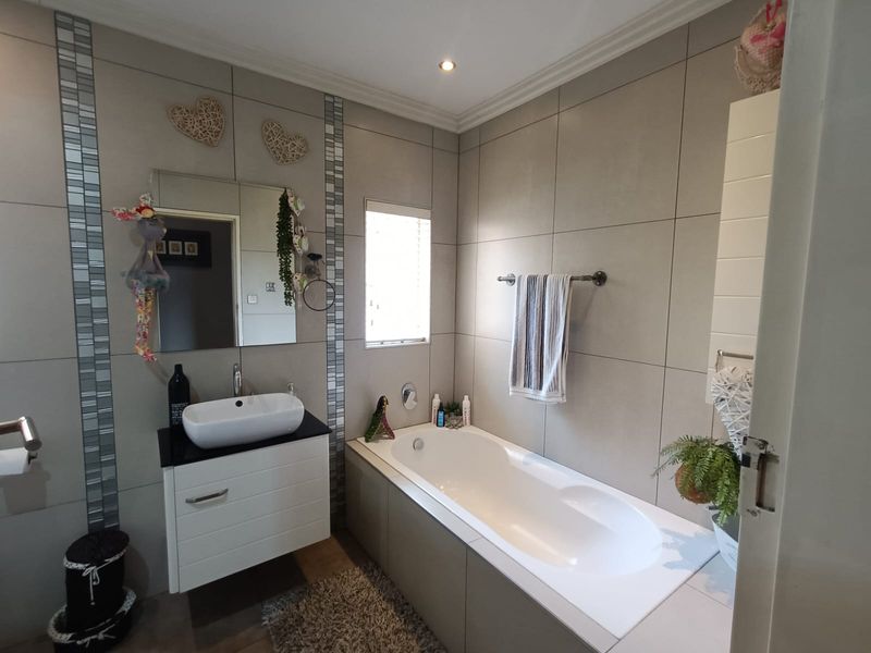 Modern bathroom featuring a vessel sink on a vanity cabinet, a built-in bathtub, and neutral wall tiling.