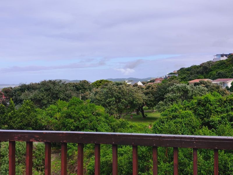 A scenic elevated view overlooking lush green trees and surrounding residential properties, framed by a wooden balcony balustrade.