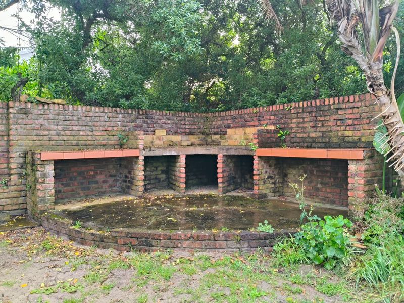 Outdoor garden area featuring a large, weathered built-in brick braai and masonry retaining wall, offering potential for a renovated entertainment space.