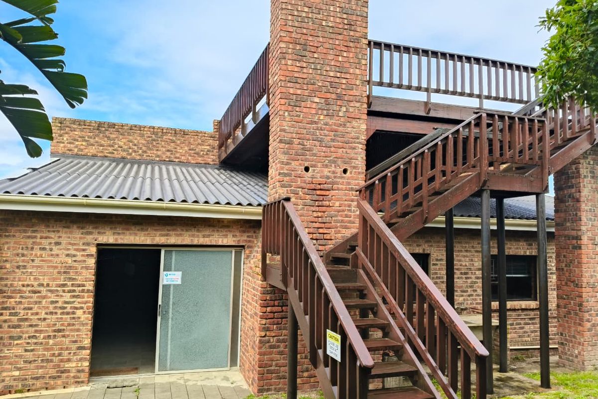 Rear exterior view featuring a brick chimney, timber staircase leading to an upper balcony, and a paved patio area with sliding door access.