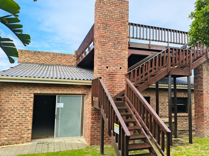Rear exterior view featuring a brick chimney, timber staircase leading to an upper balcony, and a paved patio area with sliding door access.