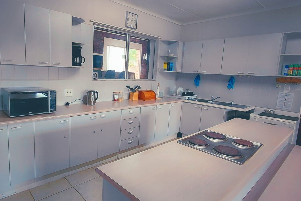 A functional kitchen featuring ample built-in cabinetry, laminate countertops, a central island with an electric hob, and a tiled backsplash.