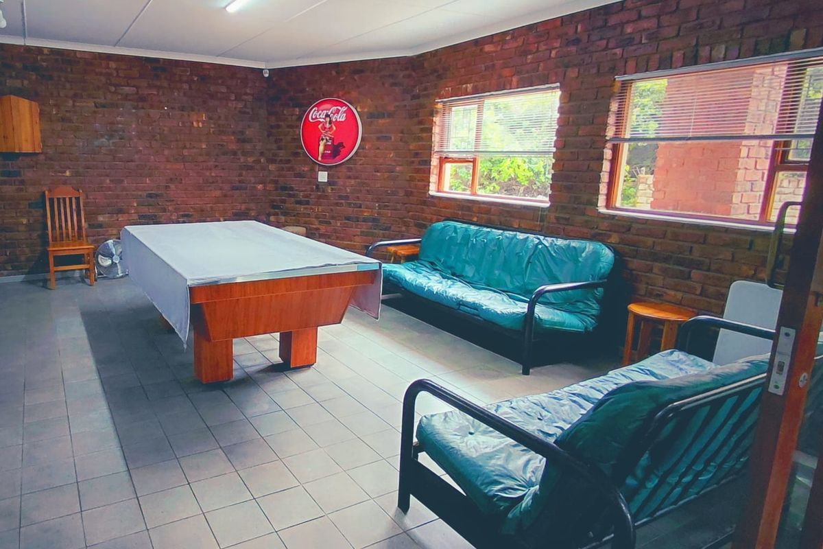 A spacious living area featuring exposed brick walls, tiled flooring, and large windows with venetian blinds, offering a rustic and functional entertainment space.