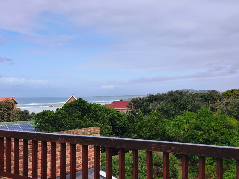 Elevated view overlooking coastal landscape and ocean, featuring a timber balustrade and brick chimney stack in the foreground.