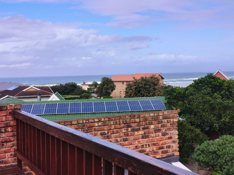 Elevated coastal view featuring a residential roof with solar panels, a brick parapet wall, and a timber balustrade overlooking the ocean.
