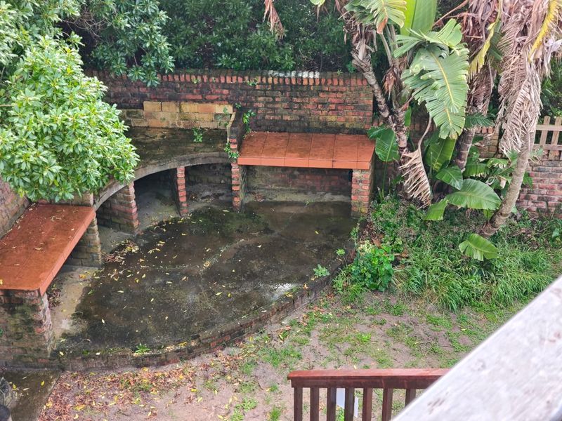 An outdoor rear area featuring a built-in brick braai and concrete patio, currently showing significant signs of weathering and requiring maintenance.