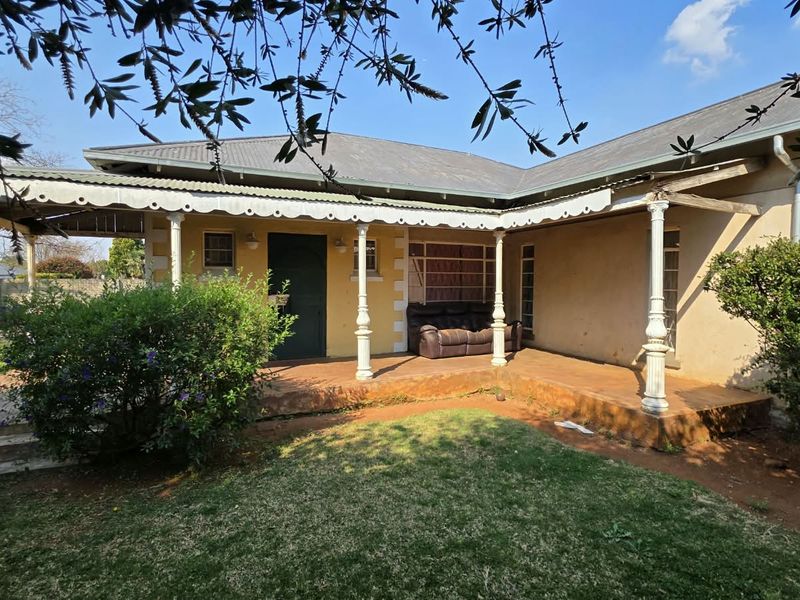 A covered wrap-around veranda featuring decorative metal columns and a corrugated roof, overlooking a private garden area.