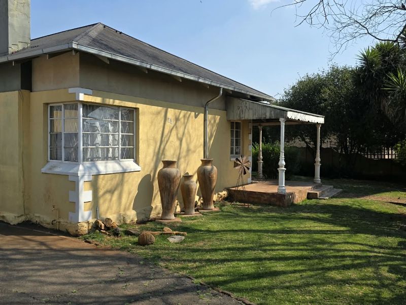 A side view of a single-story house featuring a bay window, a covered porch area, and a chimney, set within a garden space.
