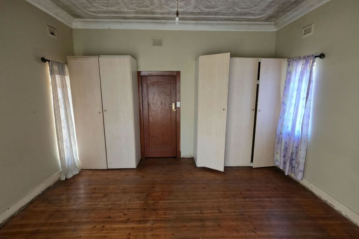 A bedroom featuring original timber flooring, ornate ceiling detailing, and built-in wardrobes flanking a central timber door.