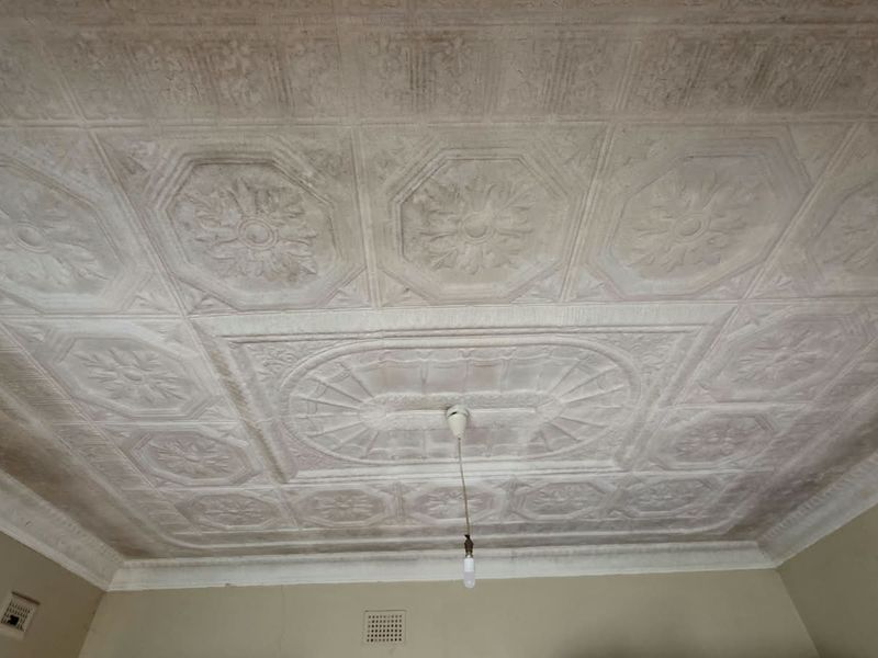 A view of an interior room featuring a decorative pressed metal ceiling with a central rose and pendant light fitting, showing signs of age.