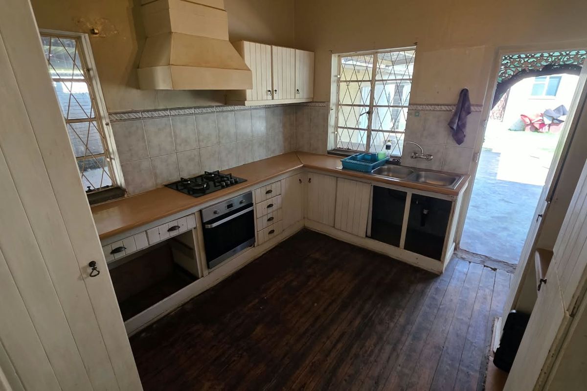 A dated kitchen featuring built-in cabinetry, a gas hob, oven, and extractor hood, with timber flooring and direct access to the exterior.