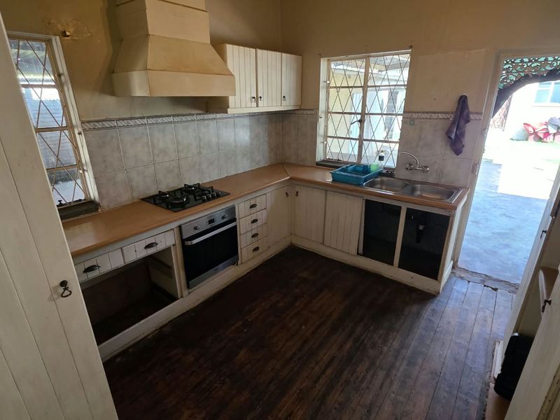 A dated kitchen featuring built-in cabinetry, a gas hob, oven, and extractor hood, with timber flooring and direct access to the exterior.