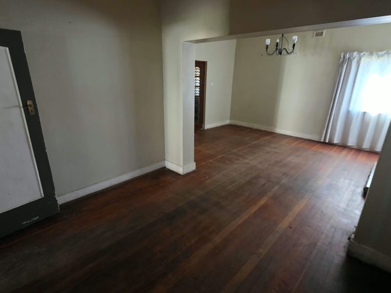 An empty living area featuring original hardwood flooring, neutral walls, and a classic archway connecting to an adjacent space.