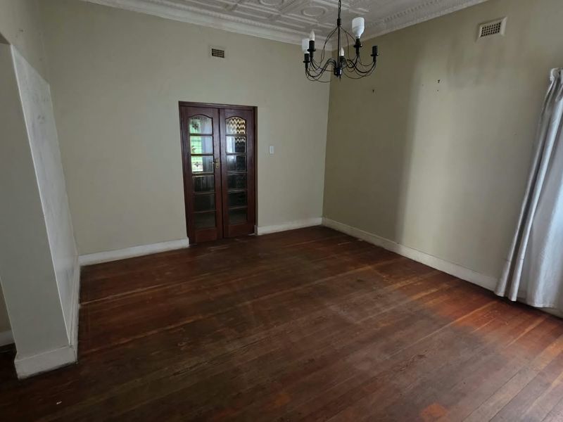 An empty living room featuring original timber flooring, decorative ceiling detailing, and classic French doors, offering a blank canvas for renovation.