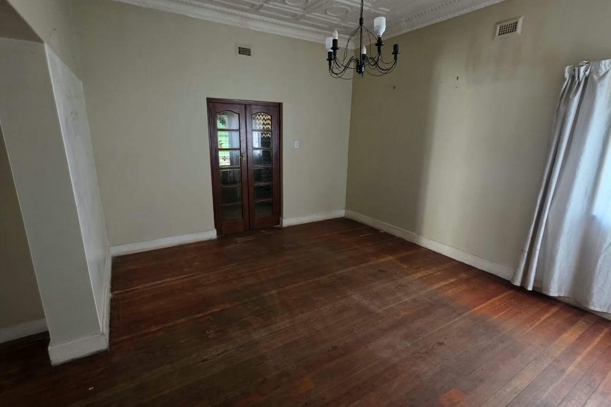 An empty living room featuring original timber flooring, decorative ceiling detailing, and classic French doors, offering a blank canvas for renovation.