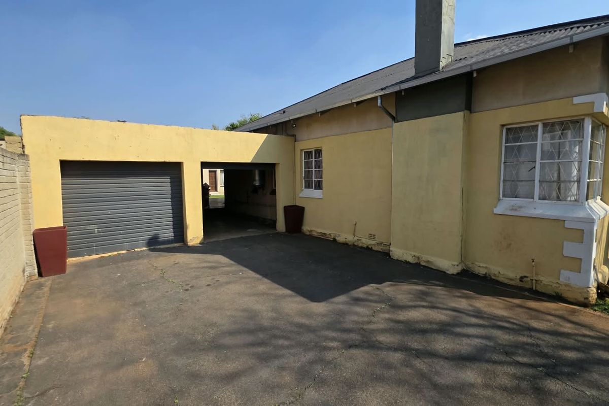 Rear exterior view of the property featuring a single garage, asphalt driveway, and a bay window with visible wear to the exterior wall finishes.