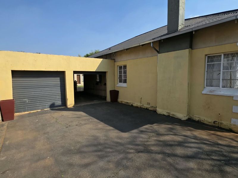 Rear exterior view of the property featuring a single garage, asphalt driveway, and a bay window with visible wear to the exterior wall finishes.
