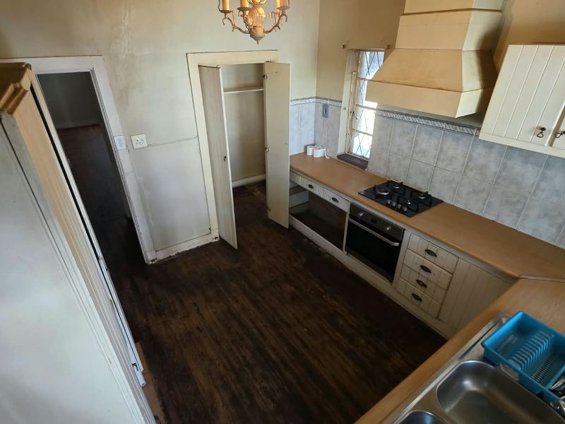 A dated kitchen featuring built-in cabinetry, a gas hob, and an oven, requiring cosmetic updates and flooring restoration to modernize the space.
