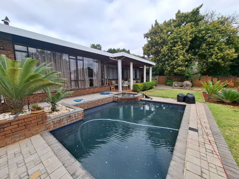 Rear exterior view featuring a swimming pool, paved surround, and a covered patio area adjacent to the main house structure.