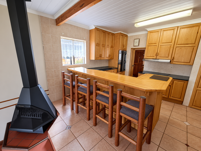 Kitchen featuring wooden cabinetry, a breakfast bar, tiled flooring, and a prominent freestanding fireplace, offering a functional layout with ample storage.