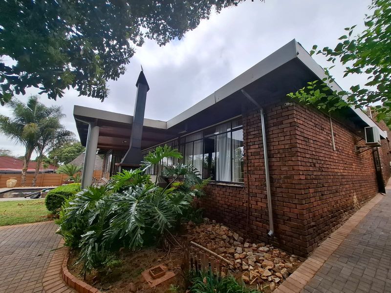 Rear view of the house featuring a brick facade, a covered patio area with an outdoor fireplace, and paved garden pathways.