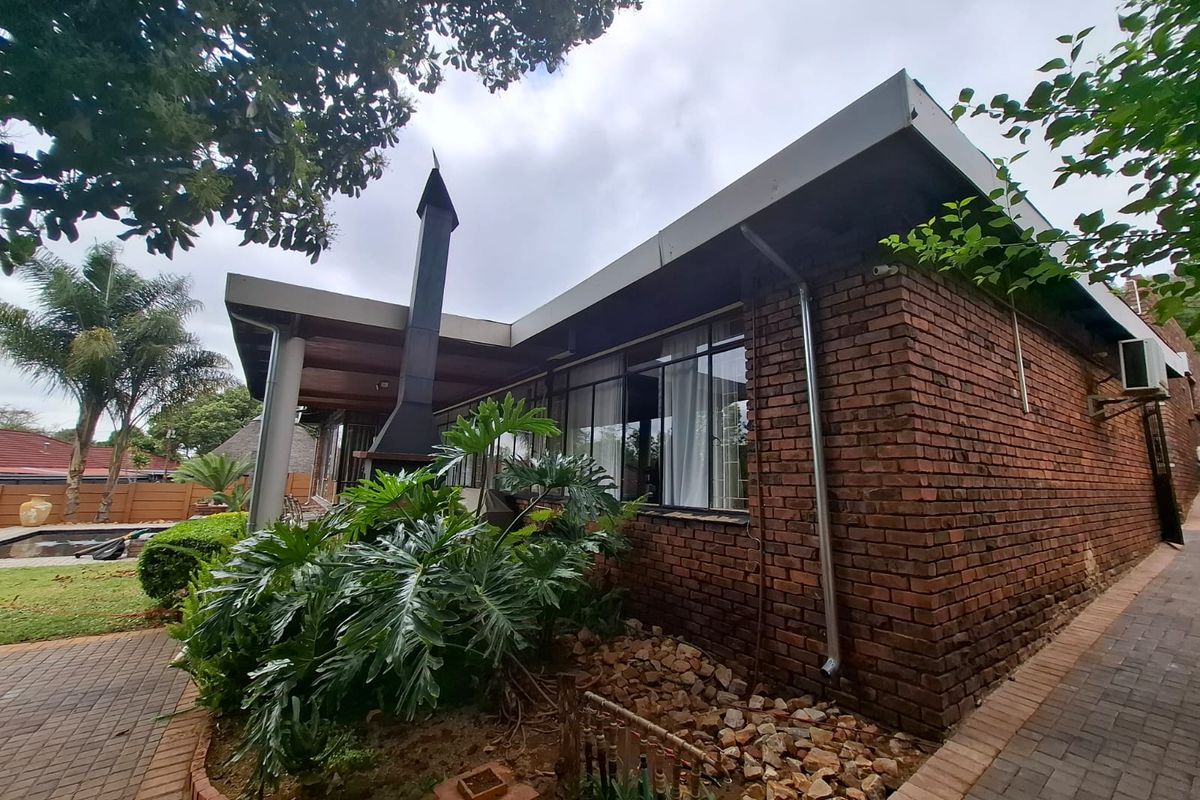Rear view of the house featuring a brick facade, a covered patio area with an outdoor fireplace, and paved garden pathways.