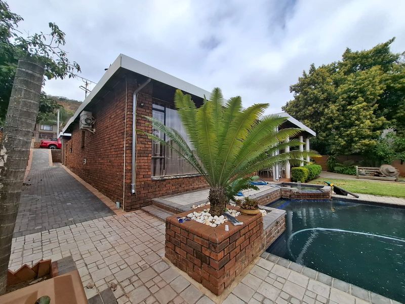 Exterior view of a brick house featuring a swimming pool, paved patio area, and a raised brick planter with a cycad.