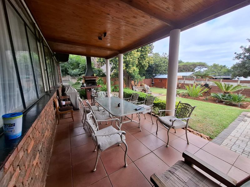 A spacious covered patio featuring tiled flooring, a timber ceiling, and a built-in braai, overlooking a well-maintained garden area.