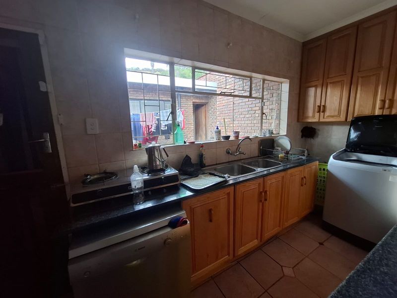 A functional kitchen featuring wooden cabinetry, tiled backsplash, double basin sink, and built-in hob, offering a practical layout with potential for modern updates.