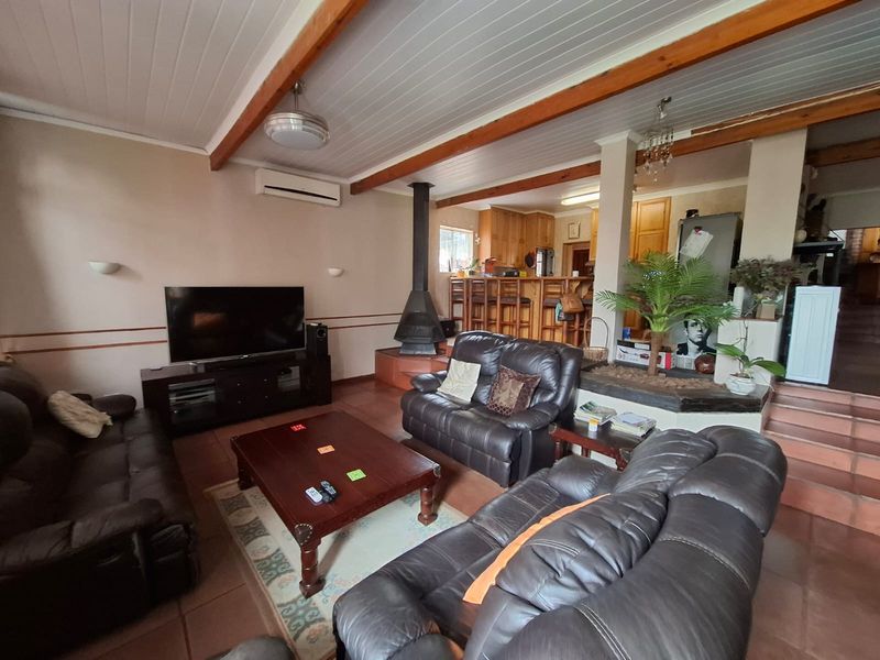 Open-plan living area featuring exposed timber ceiling beams, a freestanding fireplace, and a connected kitchen with a breakfast bar and tiled flooring.