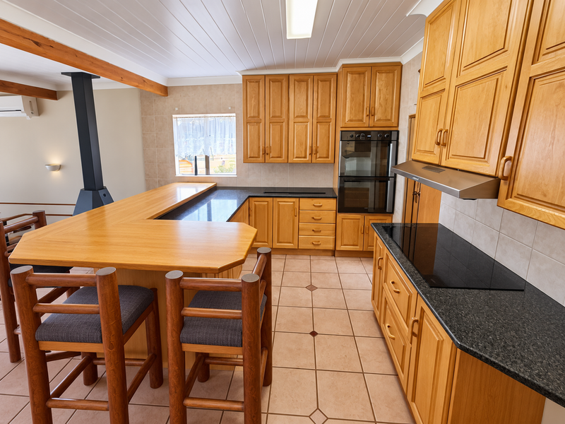 Spacious open-plan kitchen featuring warm wooden cabinetry, granite countertops, built-in double oven, induction cooktop, and a cozy wood-burning fireplace.