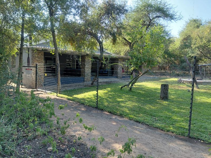 Rear view of the property featuring a covered patio with stone pillars, a well-maintained lawn, and secure perimeter electric fencing.