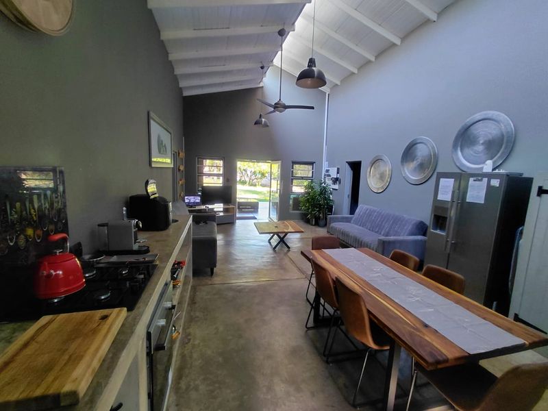 Spacious open-plan living area featuring high exposed beam ceilings, polished concrete floors, and a modern kitchen with built-in appliances.