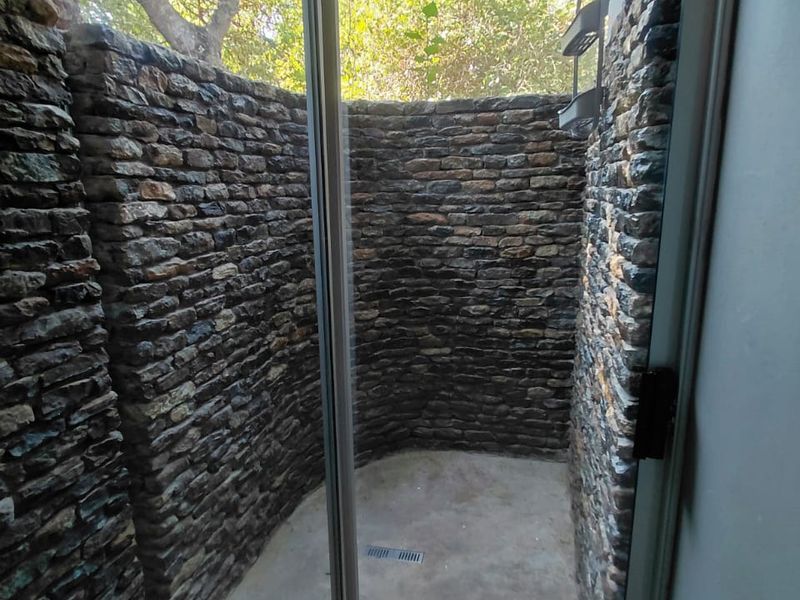 An outdoor-style shower enclosure featuring rustic stone wall cladding, a modern rain shower head, and a concrete floor with a linear drain.
