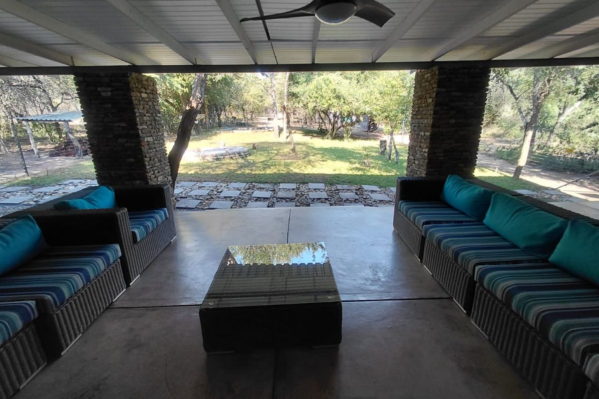 A covered outdoor patio featuring stone pillars, a ceiling fan, and concrete flooring, overlooking a spacious garden area.