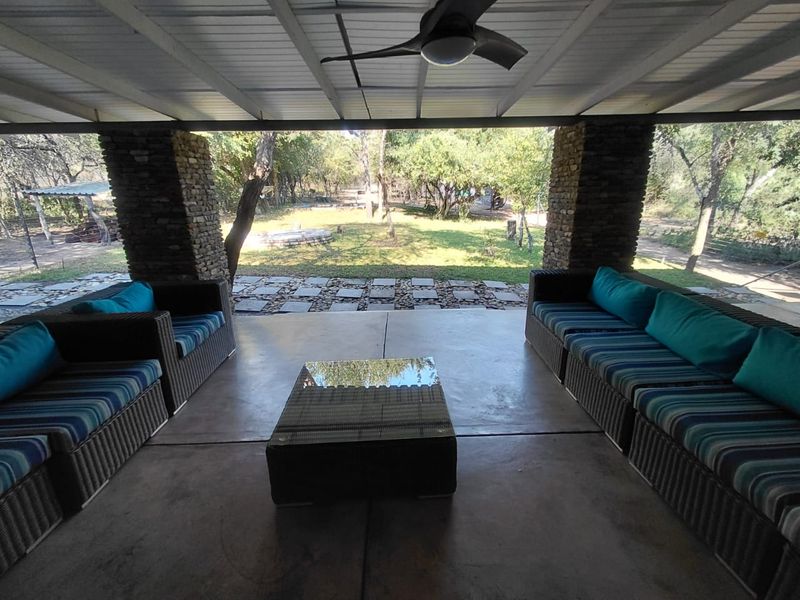 A covered outdoor patio featuring stone pillars, a ceiling fan, and concrete flooring, overlooking a spacious garden area.