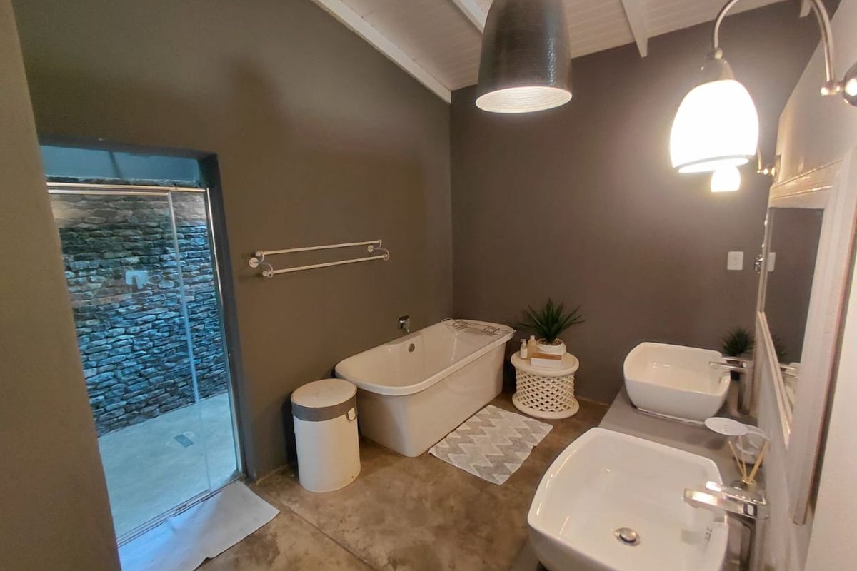Modern bathroom featuring a freestanding bathtub, double vessel sink vanity, and exposed beam ceiling with access to an outdoor area.