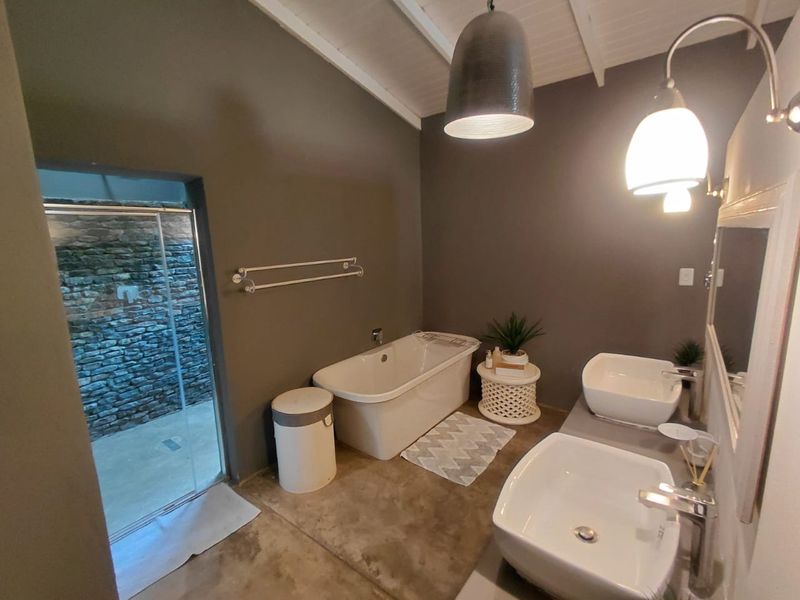 Modern bathroom featuring a freestanding bathtub, double vessel sink vanity, and exposed beam ceiling with access to an outdoor area.