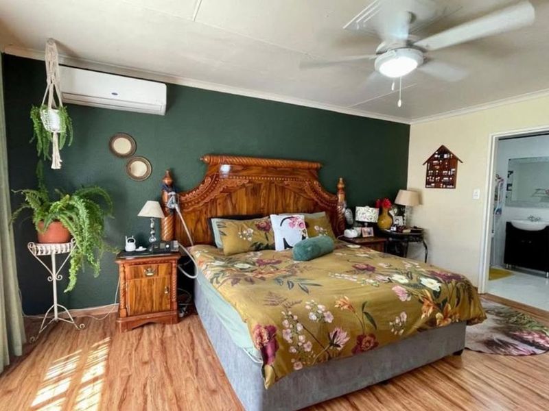 A well-maintained bedroom featuring laminate flooring, a ceiling fan, and a wall-mounted air conditioning unit, with direct access to an en-suite bathroom.