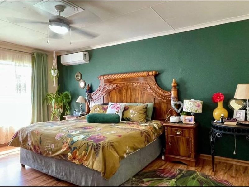 A well-maintained bedroom featuring a ceiling fan, split-system air conditioning, and laminate flooring with a bold green accent wall.