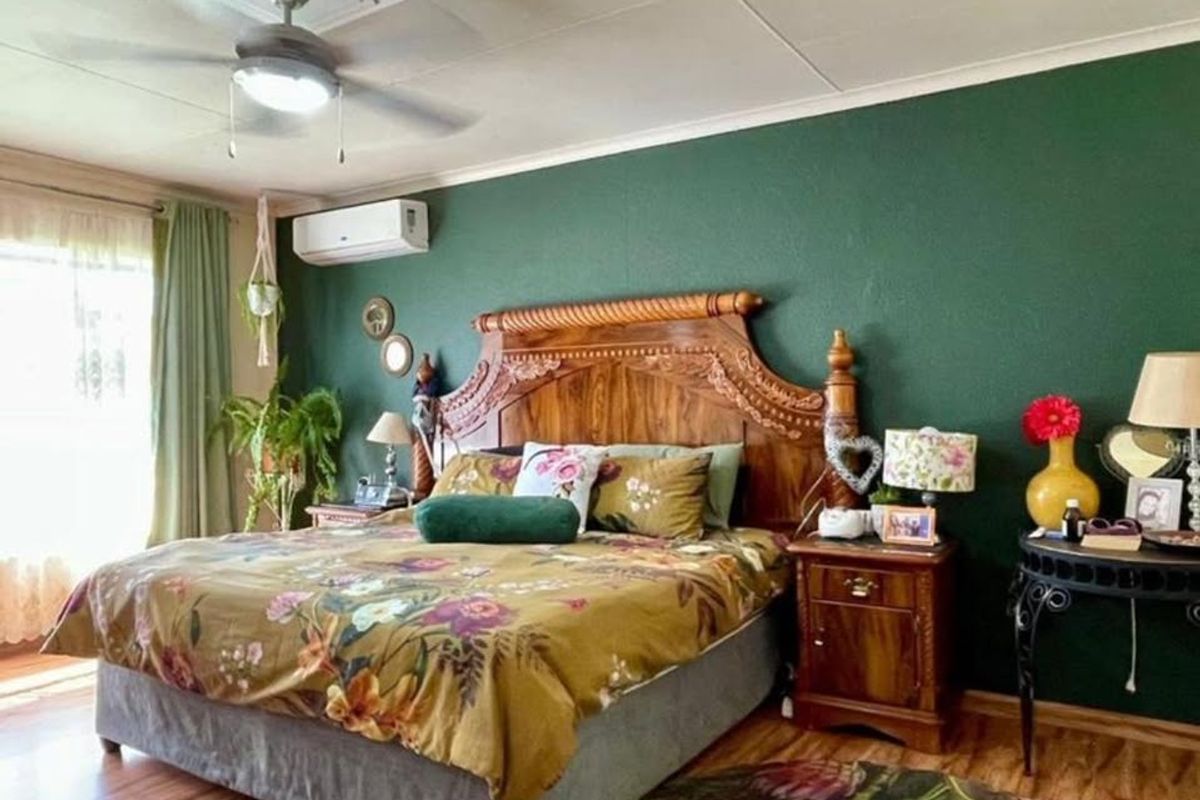 A well-maintained bedroom featuring a ceiling fan, split-system air conditioning, and laminate flooring with a bold green accent wall.